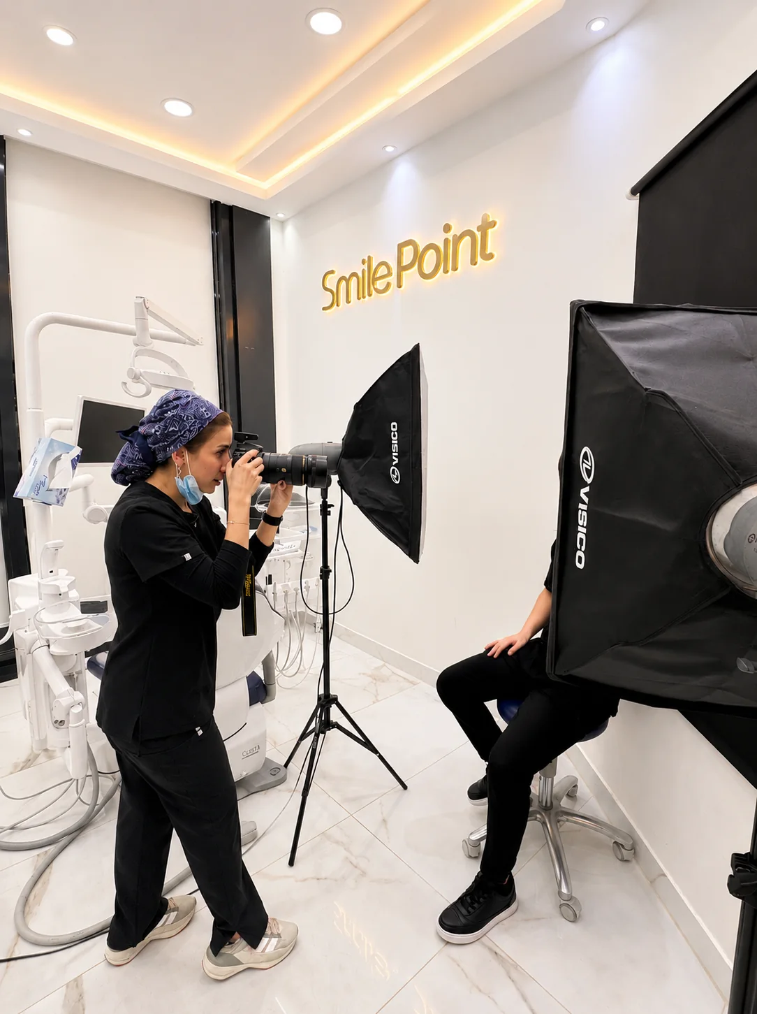Dr Amna Ali taking clinical photographs at Smilepoint, with the Smilepoint logo on the wall behind her