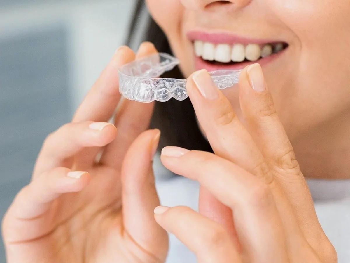 A smiling woman holding a clear aligner