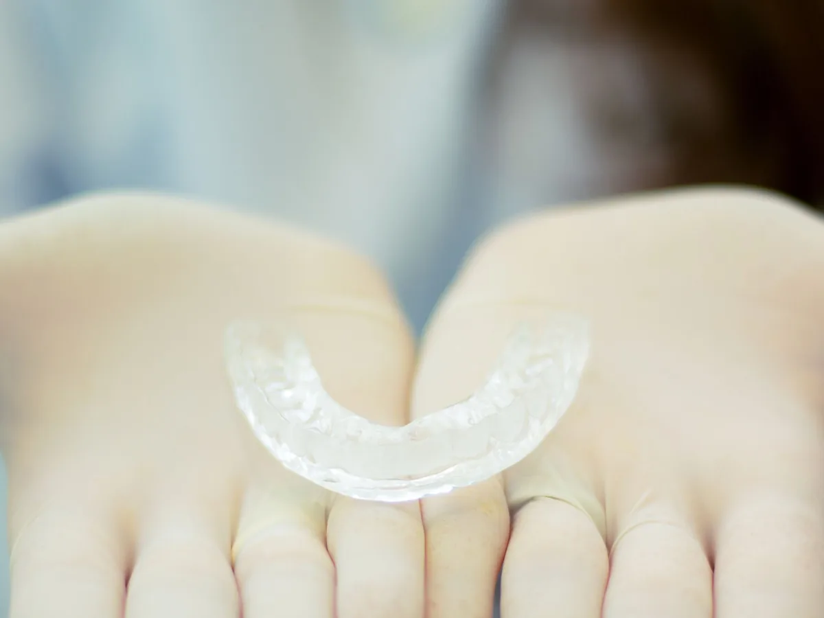 A clear removable retainer held in gloved hands