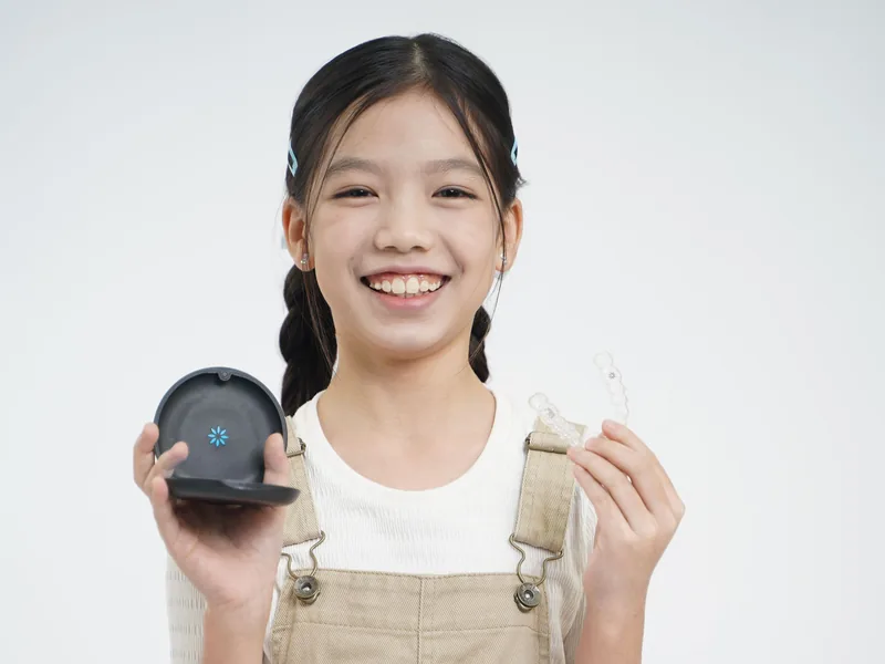 A smiling child holding a clear aligner and its case