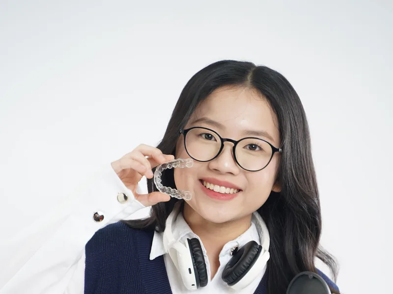 A smiling teenager holding a clear aligner and its case